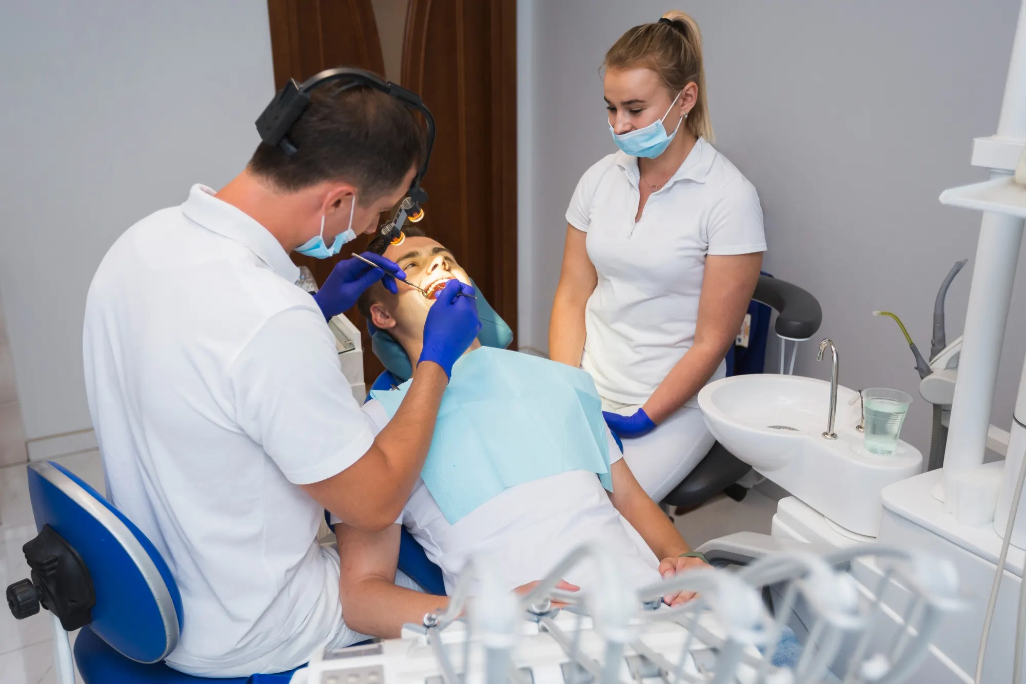 Two clinicians attend to a patient reclined in the dental chair during a consultation